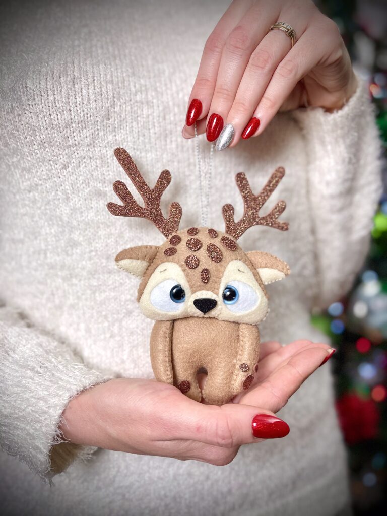 Hand holding handmade felt reindeer ornament with glitter felt antlers, showing festive felt details used for Christmas plush decorations