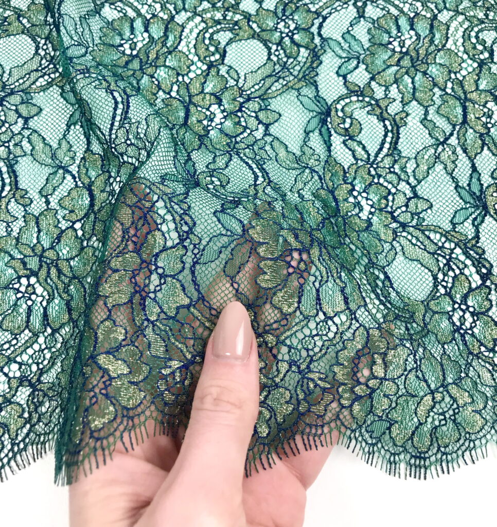 Hand holding green floral lace fabric with scalloped edge, ideal for lingerie sewing and lace appliqué projects.