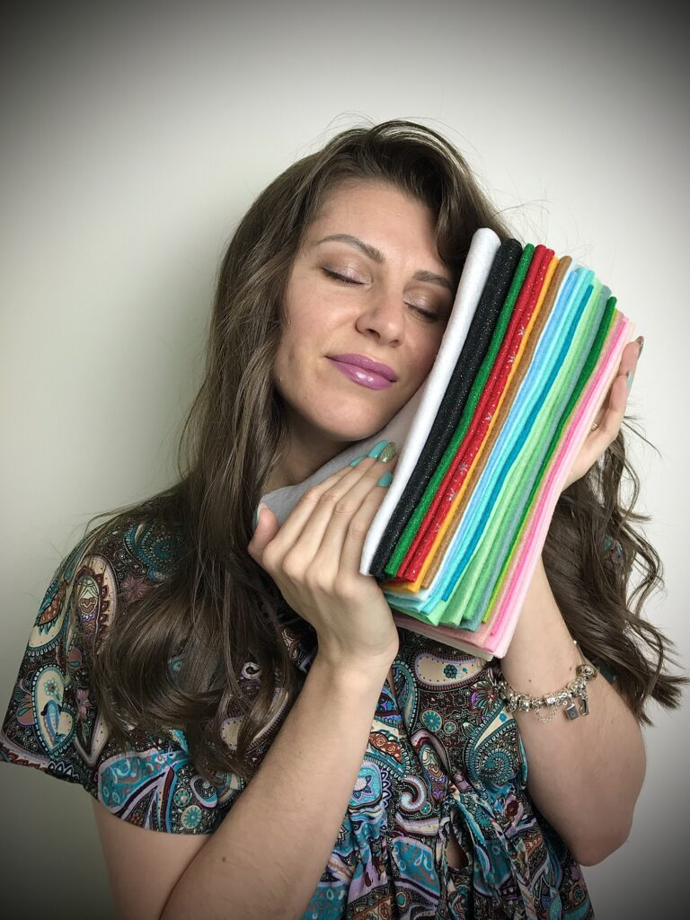 Woman holding colourful felt sheets to her face, highlighting softness and versatility of felt for sewing and craft projects