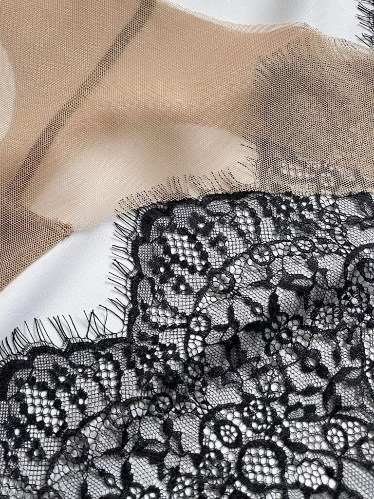 Black floral stretch lace and beige mesh fabric arranged on white background for lingerie sewing projects