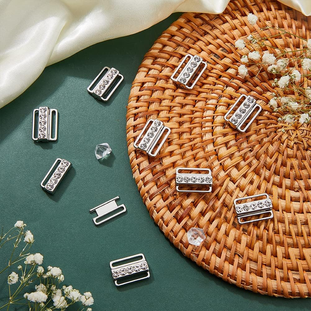Silver rhinestone lingerie buckles displayed on a green surface and wicker mat, styled with flowers and satin fabric.