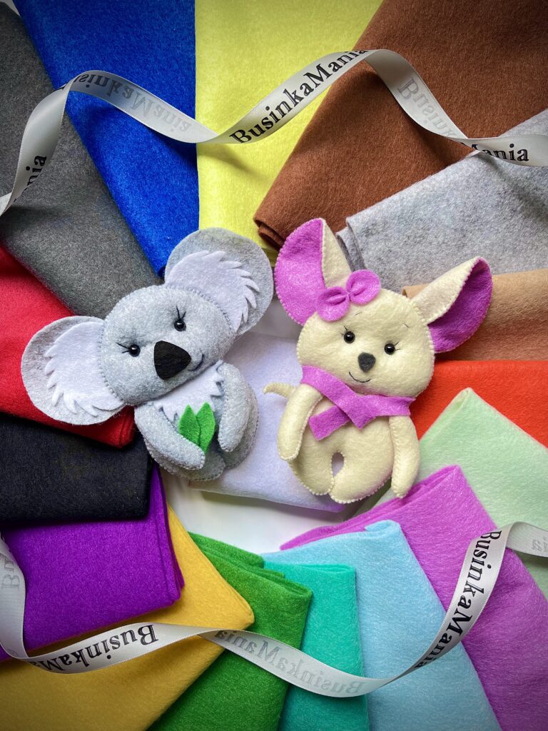 Handmade felt koala and mouse toys displayed on colourful felt sheets with BusinkaMania ribbons in the background.