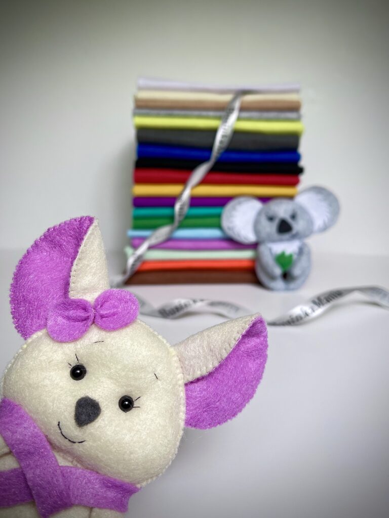 Handmade felt mouse and koala toys displayed with a colourful stack of soft felt sheets in the background.