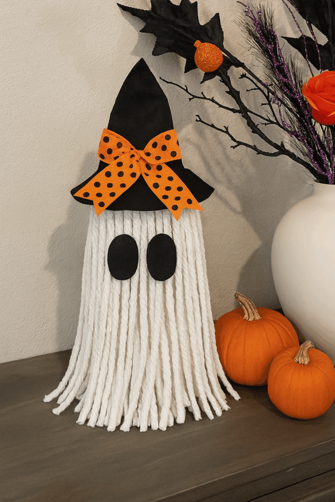 DIY no-sew yarn ghost lamp with witch hat and bow — glowing Halloween craft made with mop head, felt, and LED light for kids' decor.