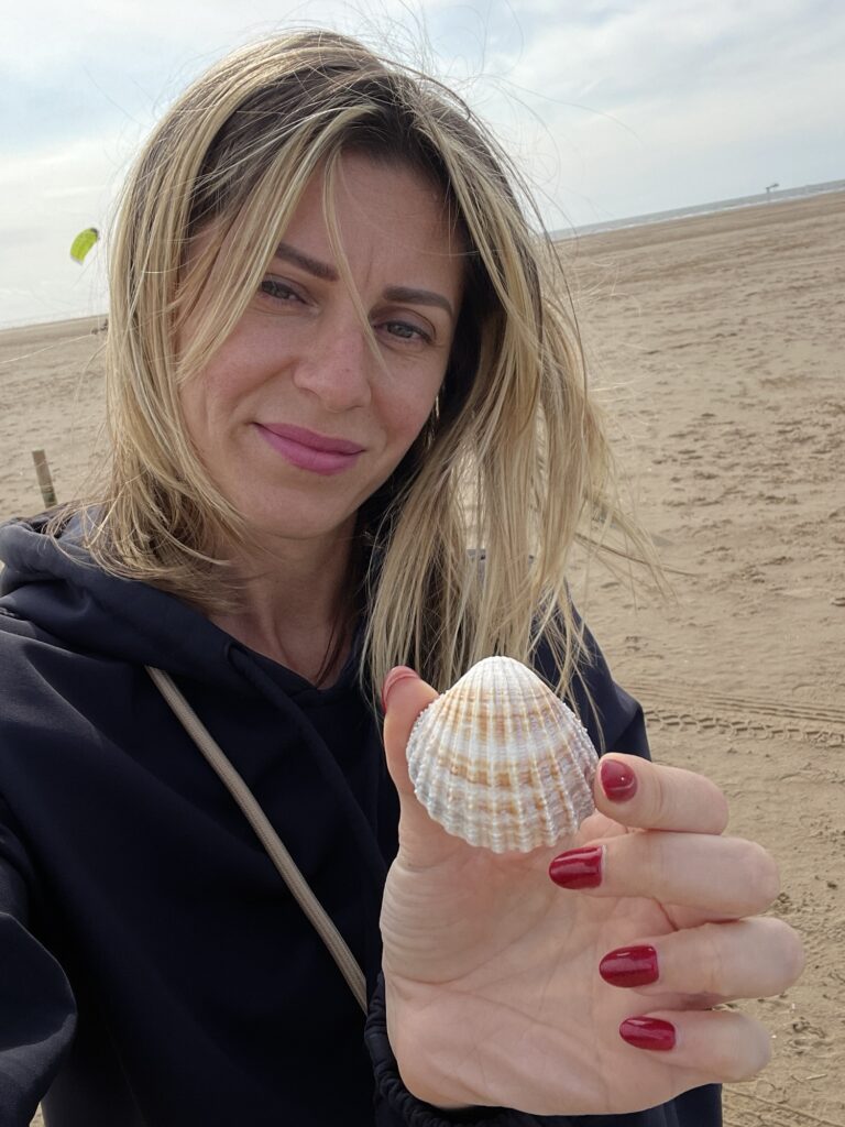 Woman holding a shell on the beach — showcasing nature finds used for DIY Halloween decorations made from repurposed materials.