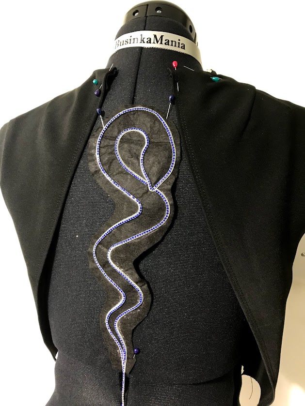Black felt garment pinned on dress form with decorative trim, showing structure and versatility of felt for fashion design