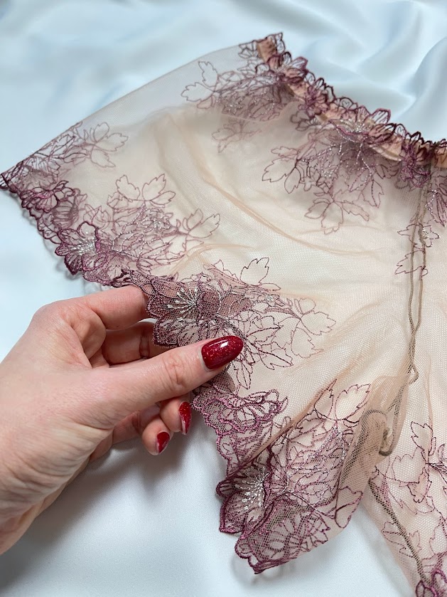 Hand holding delicate lace lingerie fabric on satin background, showing detail for sewing needle choice and fabric care.