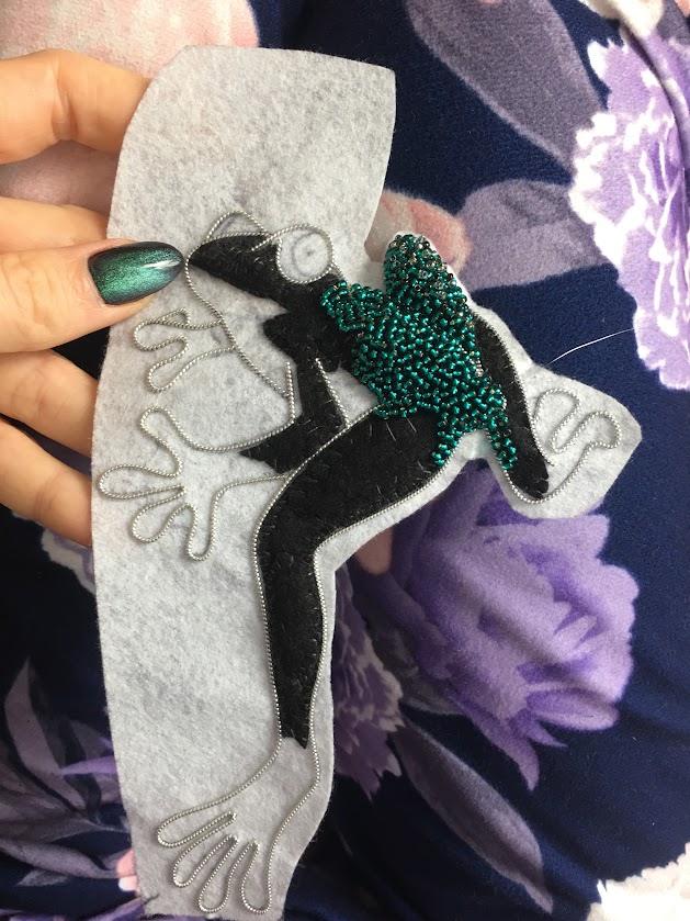Hand holding embroidered felt leapfrog patch with seed beads, showing detail and texture in beginner felt sewing project