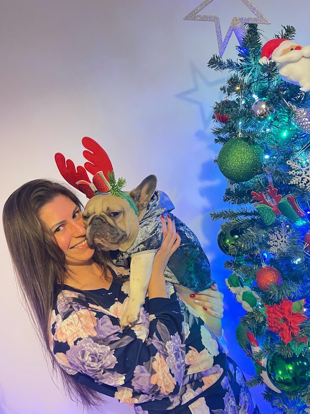 Woman with dog wearing Christmas antlers beside decorated tree, featured in DIY Christmas gifts for women craft ideas article.