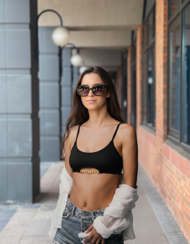 Woman wearing handmade black Top-Bra “Mia” with gold chain detail styled as a crop top with jeans and sunglasses outdoors.
