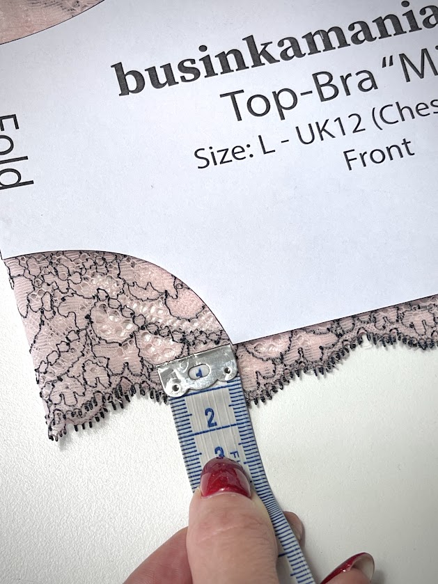 Measuring placement of Top-Bra “Mia” pattern on pink lace fabric to align the bottom edge slightly above the lace scallops.