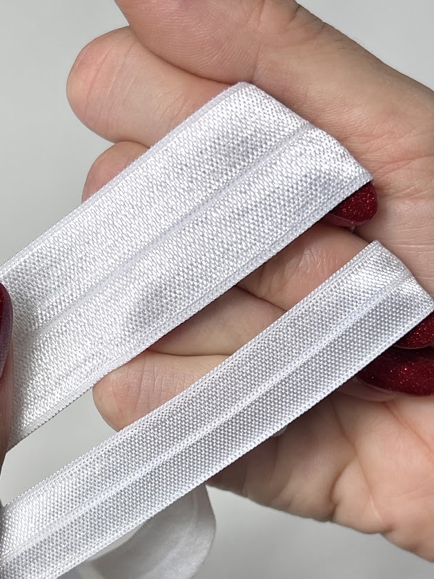 Close-up of white fold-over elastic held by hand, showing soft shiny texture used for sewing stretch swimwear edges
