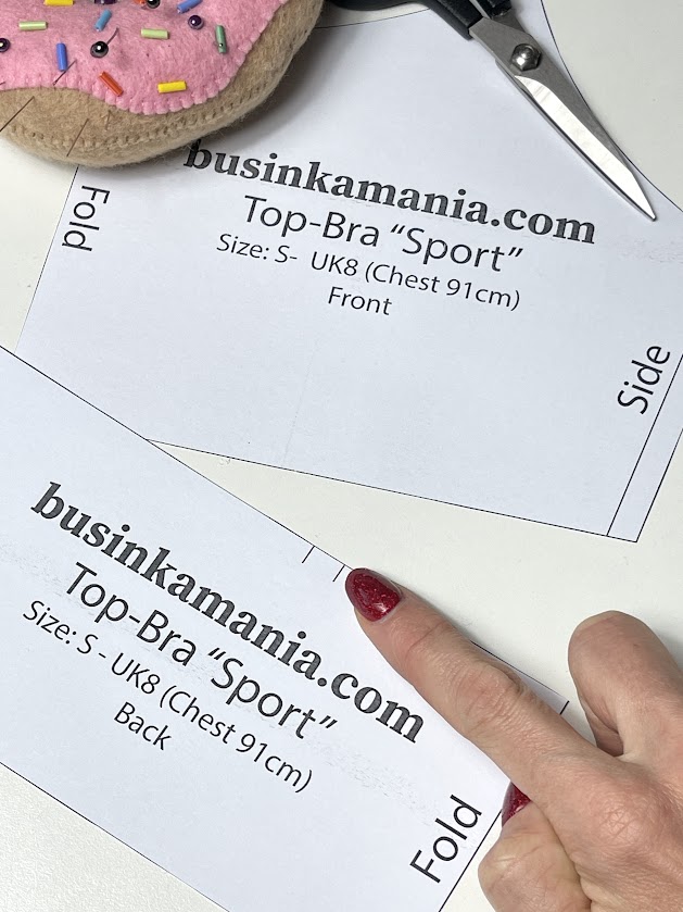 Hands holding Top-Bra “Sport” sewing pattern pieces on fabric, preparing to cut along the fold line before sewing.