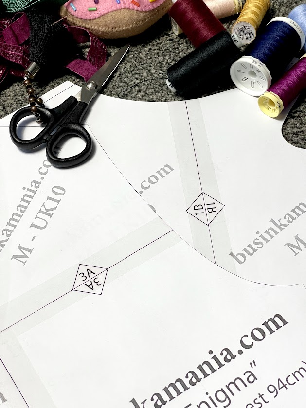 Printed Crop Top “Enigma” sewing pattern pages with triangle markers for assembly, shown with scissors, thread, and sewing supplies