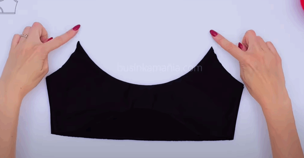 Hands holding a black handmade Top-Bra “Mia” laid flat on a table, showing the front cut-out section before adding elastic.