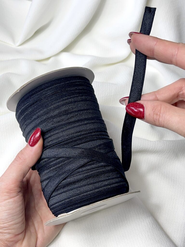 Hands holding a roll of slim black elastic used for finishing the scallop hem on the lace version of the Top-Bra “Sport”.