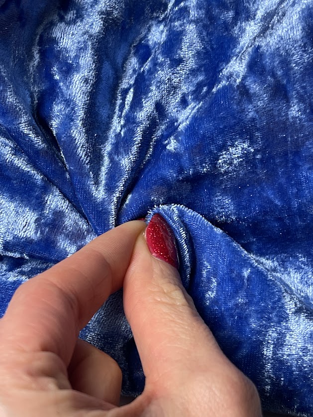 Close-up of shiny blue four-way stretch velvet fabric held by hand, showing soft luxurious texture for swimwear or beachwear sewing