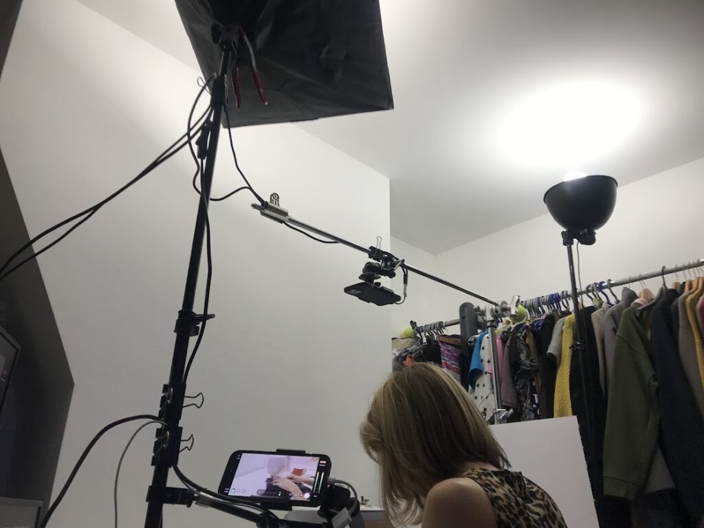 Sewist filming sewing tutorial under softbox lighting setup using tripod and C-stand to achieve smooth even light for sewing videos.