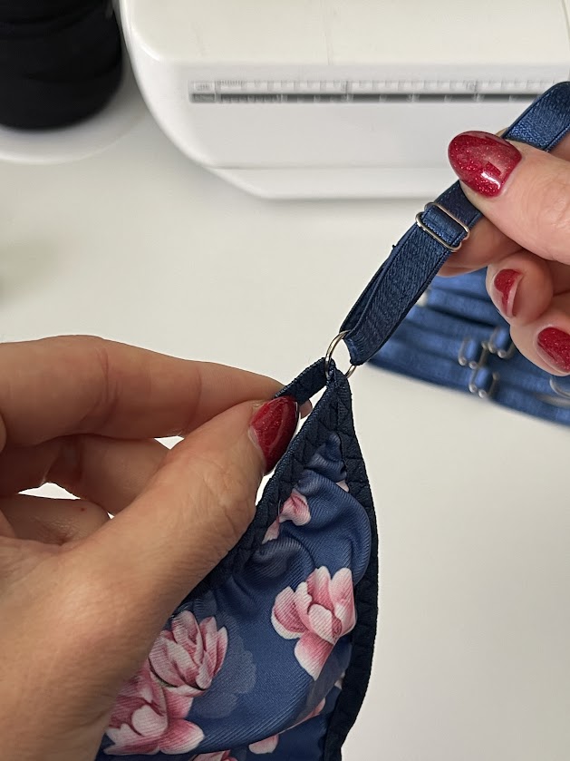 Hands attaching elastic strap with ring to blue floral thong panties near sewing machine, shown in Step 5 underwear tutorial.