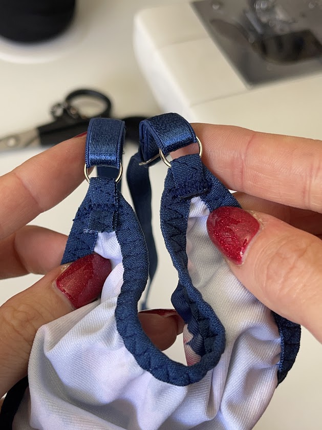 Hands holding finished blue thong panties showing attached elastic straps and rings, final step of underwear sewing tutorial.