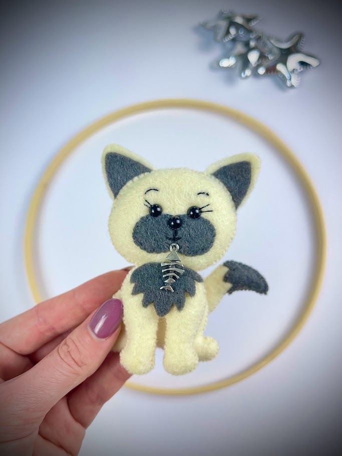 Handmade felt cat plush holding a small pendant, showing how charm accessories add personality to felt toys and plush projects