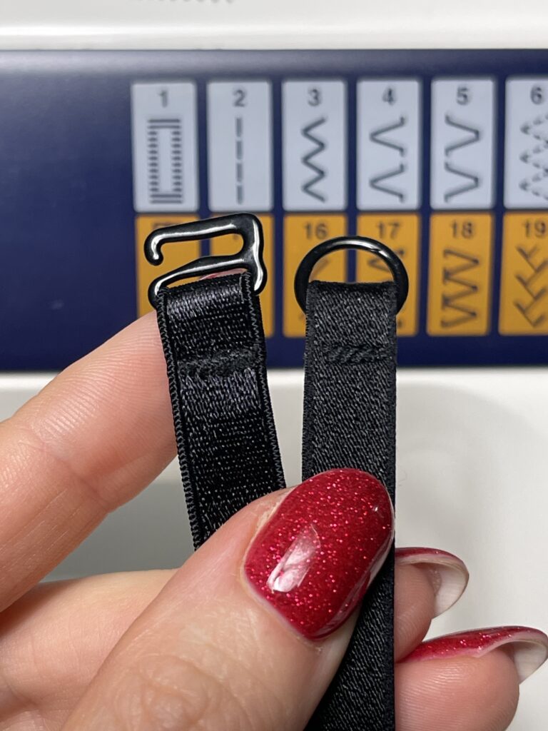 Hand holding two black bra straps with metal sliders in front of sewing machine zigzag stitch chart settings