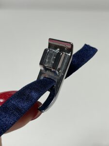 Navy lingerie elastic threaded through the central hole of a sewing machine presser foot.