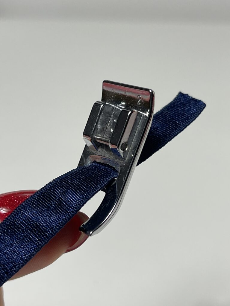 Navy lingerie elastic threaded through the central hole of a sewing machine presser foot.