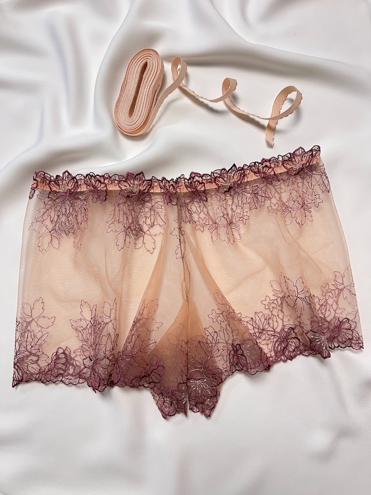 Lingerie mesh fabric with lace edge and a roll of nude lingerie elastic laid flat for sewing preparation.