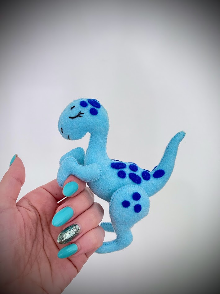 Hand holding blue felt dinosaur plush showing detailed repeating elements for craft sewing pattern testing