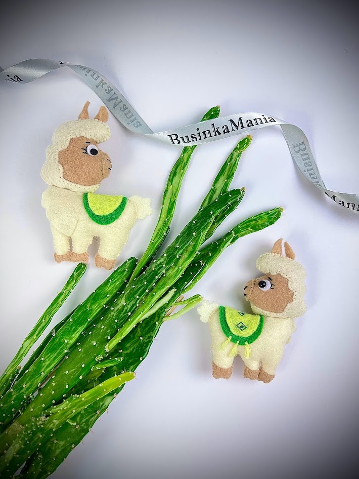 Two felt alpaca plush toys beside textured green felt leaves, BusinkaMania ribbon above, promoting free sewing pattern and craft ideas
