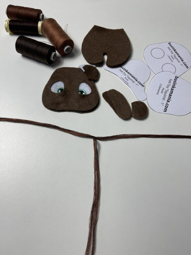 Braided thread bundle forming T shape with 30 strands each side beside felt cow pieces and sewing pattern templates.