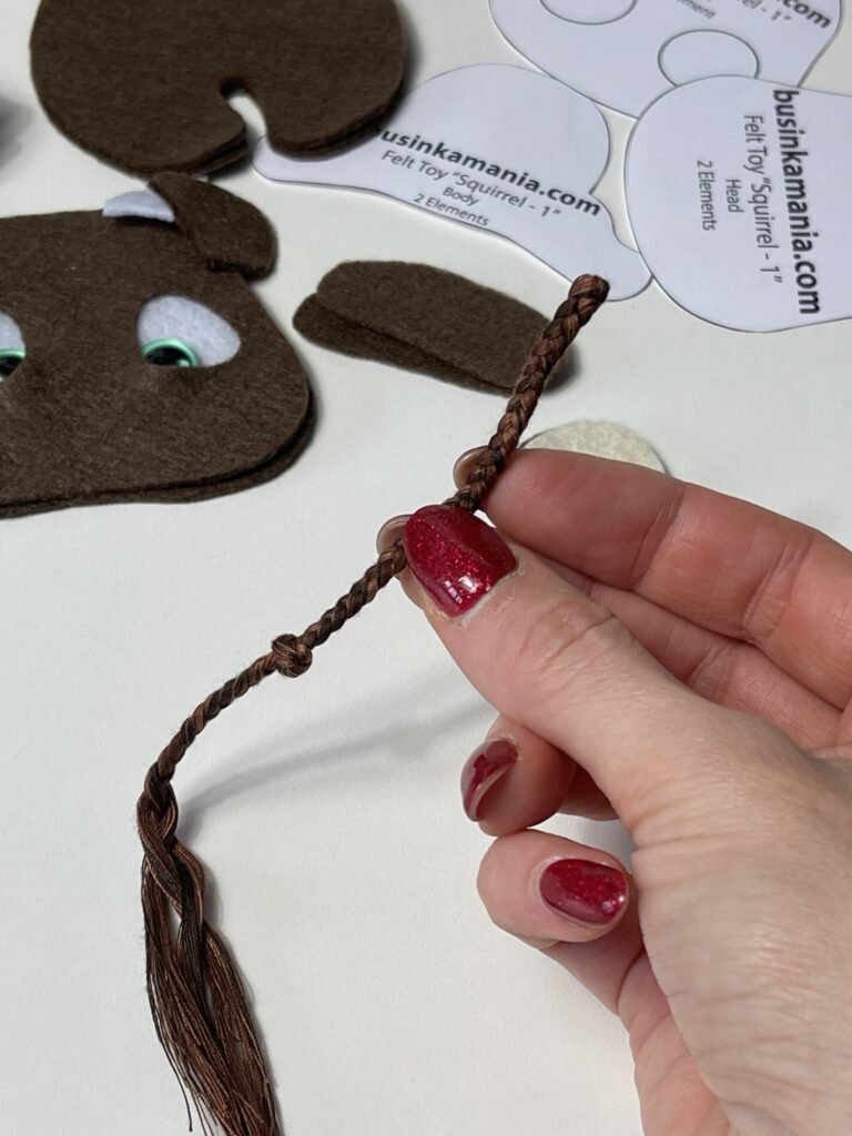 Braided tassel tail with extra 2–3 mm allowance shown before attaching to felt cow plush body pieces.