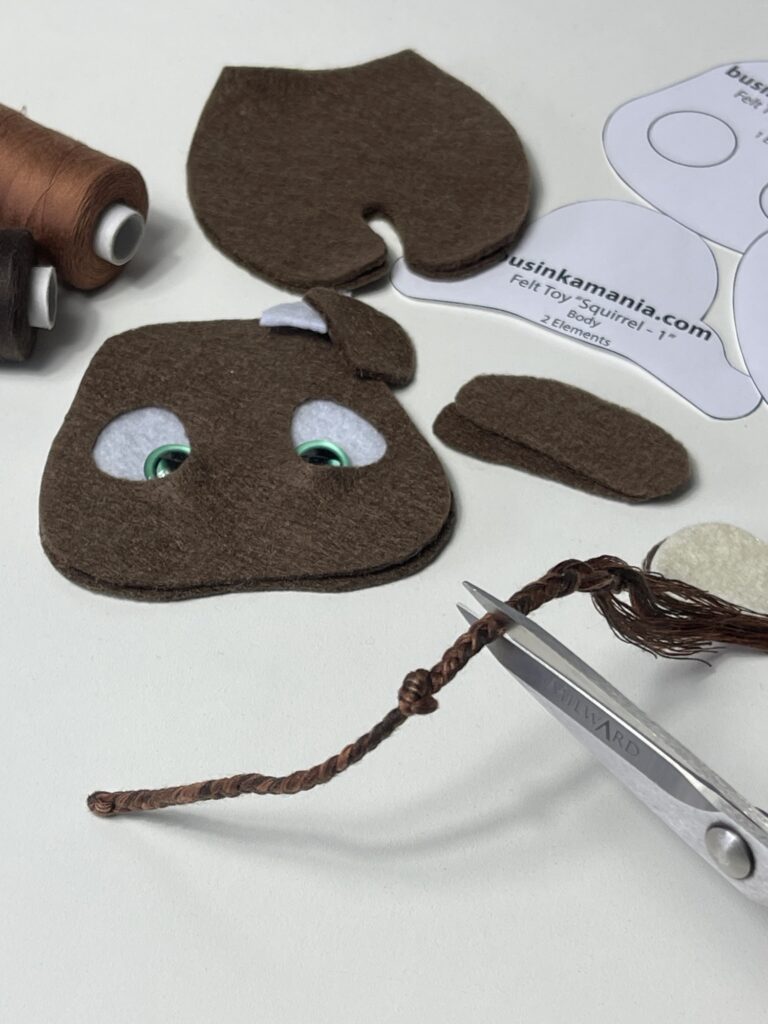 Cutting braided thread to create 2 cm tassel finish for felt cow plush tail beside pattern pieces.