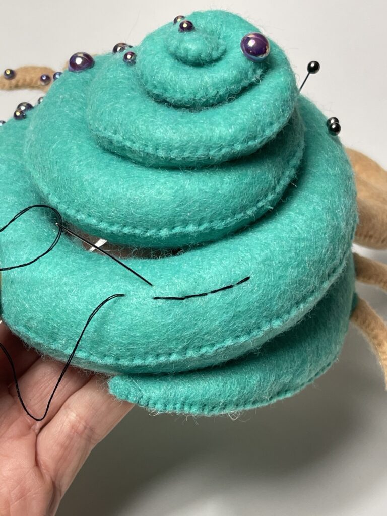 Chain stitch forming soft oval links on felt surface, needle entering slightly backward and emerging forward along design line