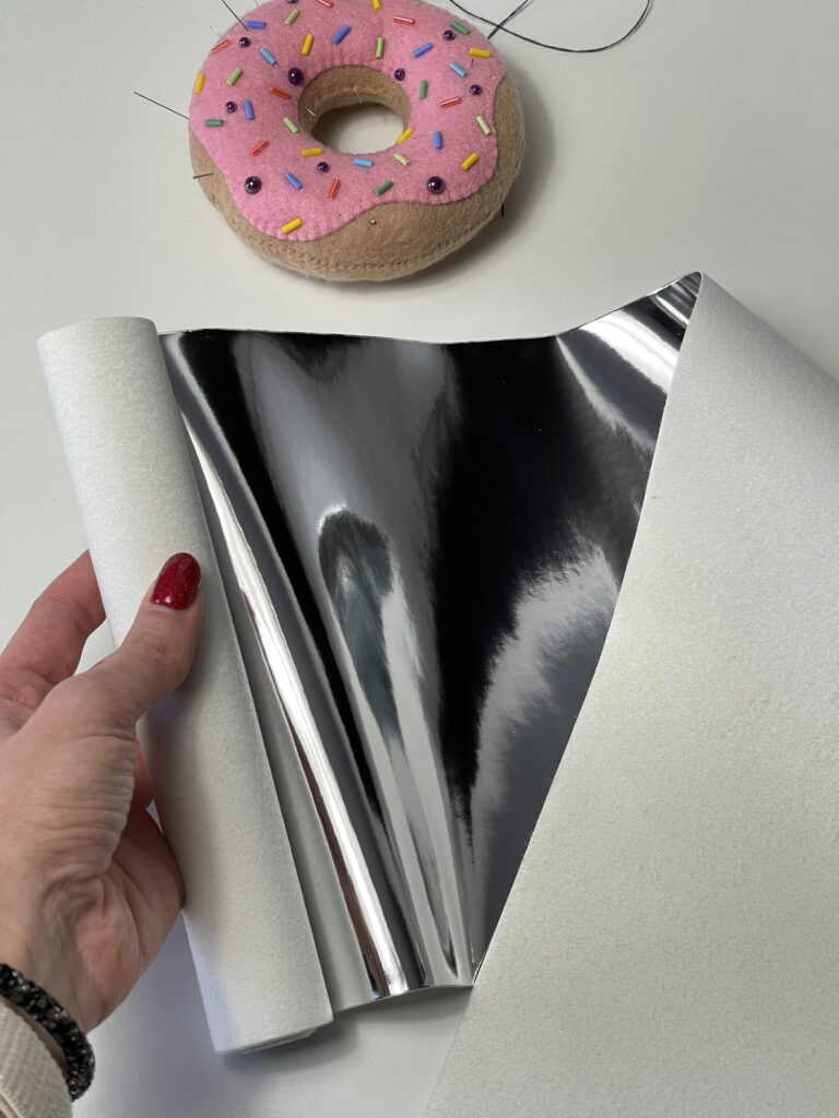 Hand holding holographic mirrored leather sheet beside felt doughnut ornament for craft and felt toy making