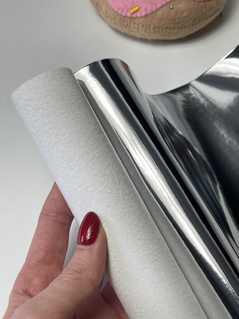 Hand holding holographic mirrored leather sheet beside felt doughnut ornament for craft and felt toy making