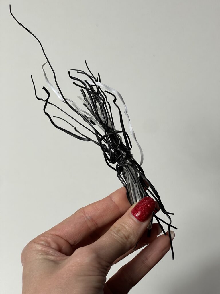 Hand holding thin craft wire pieces used inside felt plush tails for flexible shaping in DIY felt sewing projects