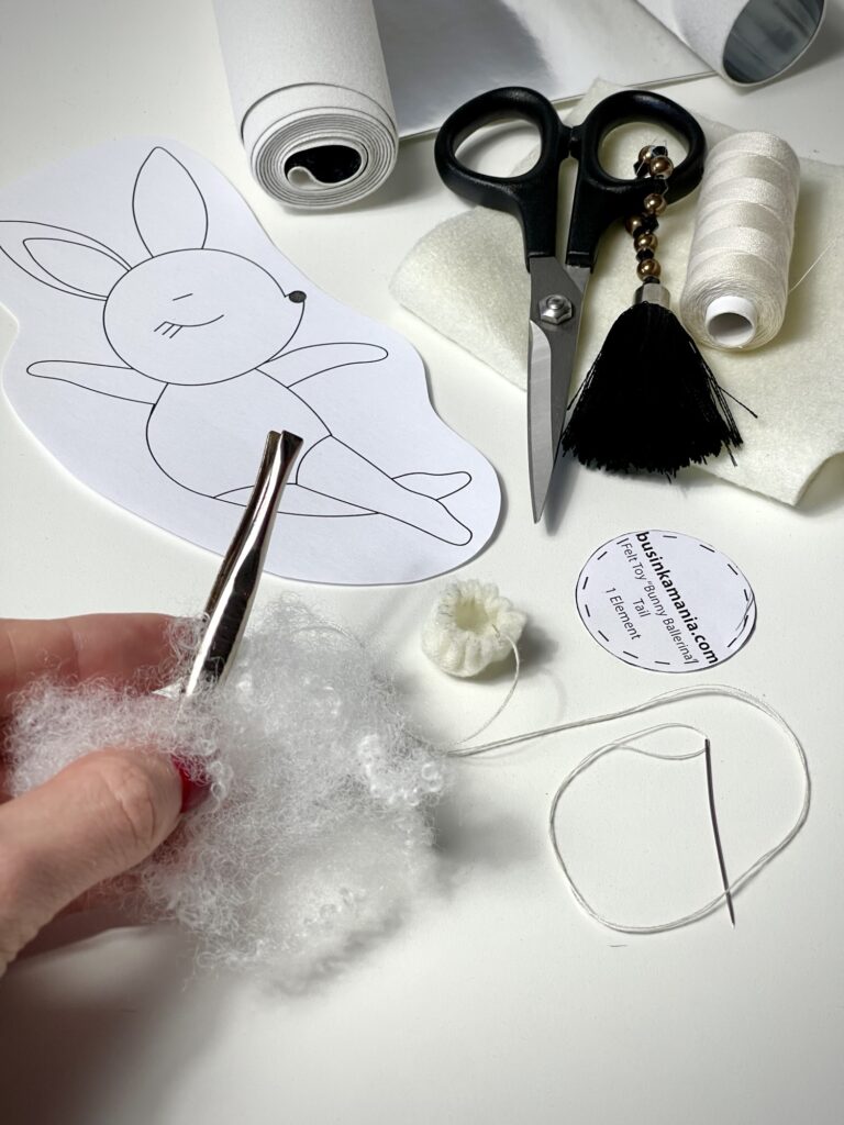 Using tweezers to stuff synthetic filling into small gathered felt circle for round 3D plush tail