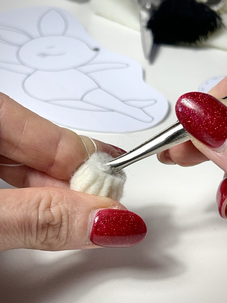 Tweezers packing synthetic filling into small gathered felt pouch to shape round 3D plush animal tail
