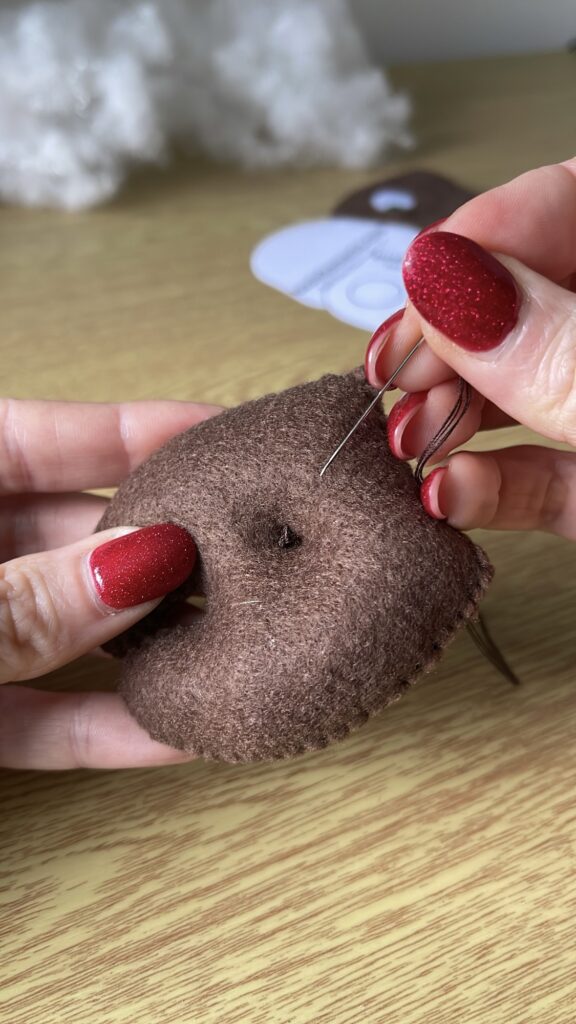 Needle inserted into back of brown felt plush to hide knot and stitches, showing technique for clean, invisible thread finish