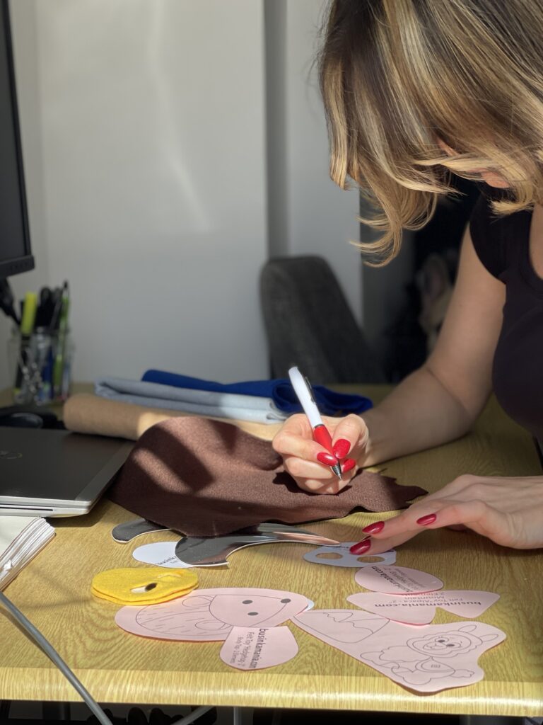 Designing felt toy pattern on fabric with pen, showing plush template pieces and careful testing process at workspace