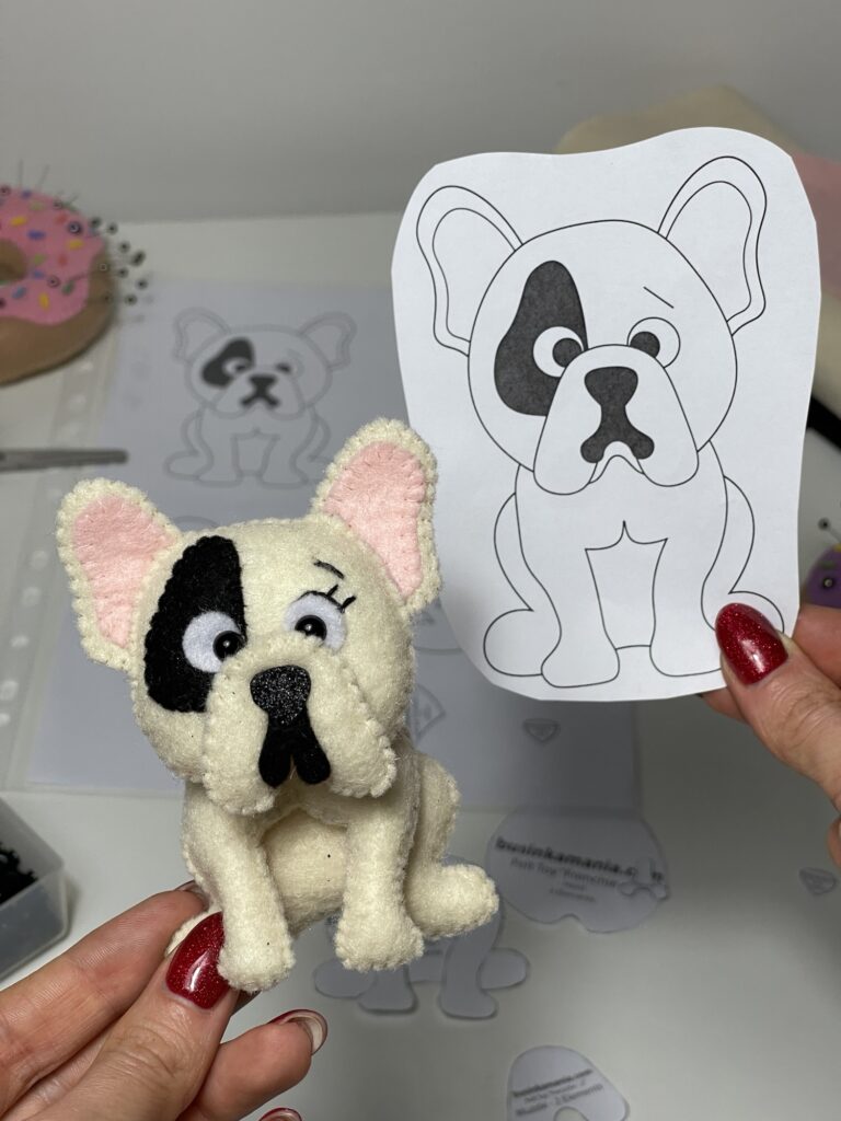 Finished felt French bulldog plushie next to original pattern drawing, showing handmade result after testing plush toy pattern