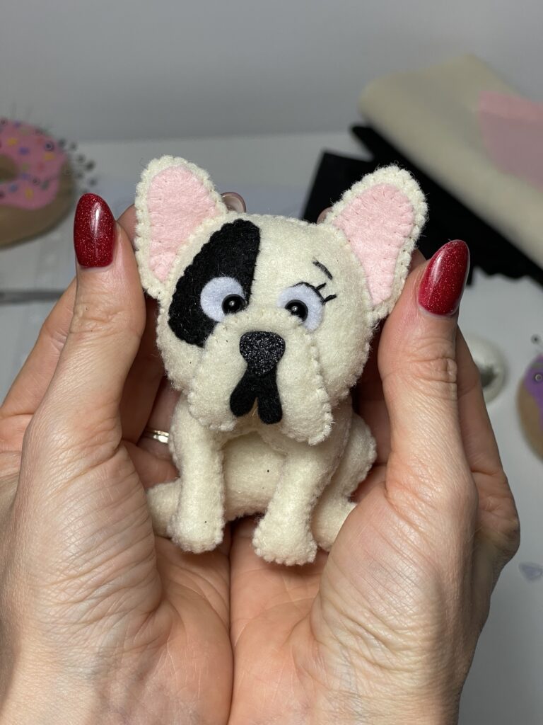 Finished felt French bulldog plushie held in hands before attaching key pendant to turn handmade toy into bag accessory