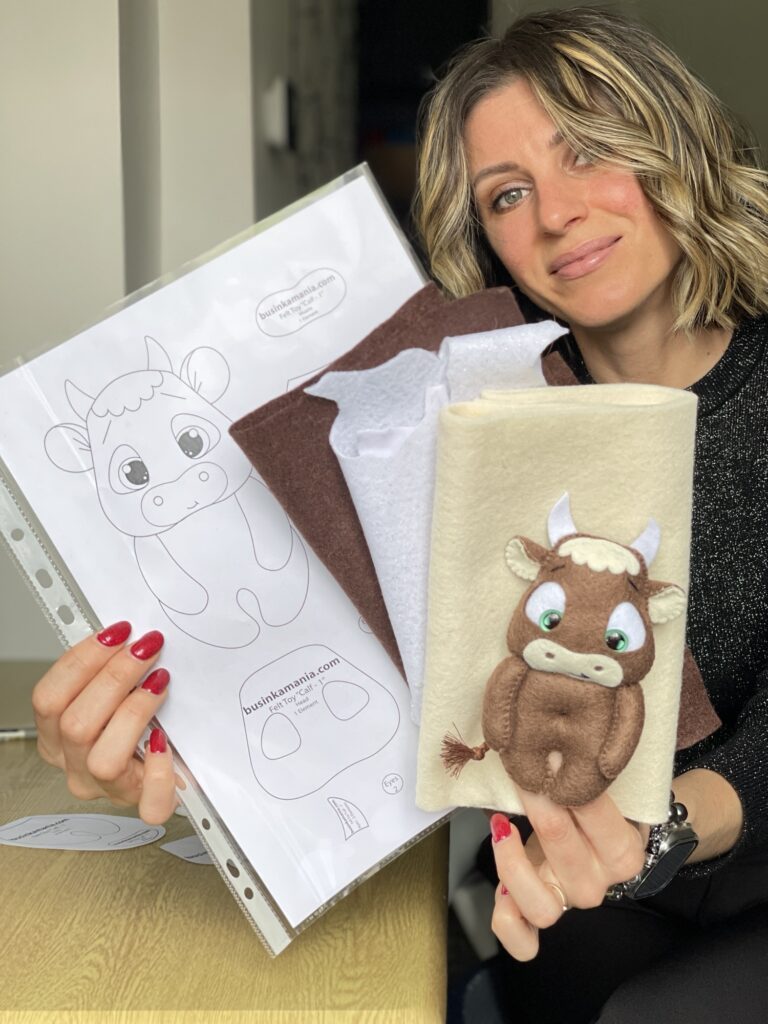 Woman holding calf plush toy and felt sewing pattern pieces, showing finished handmade plush from previous week’s project