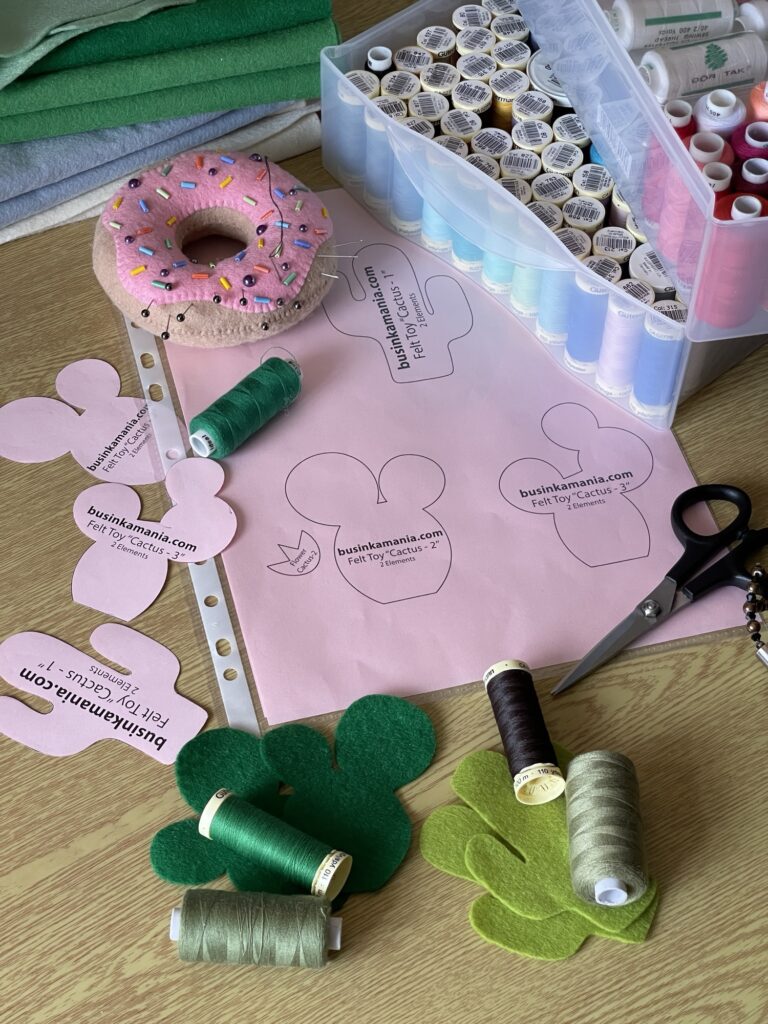 Felt cactus plush pattern pieces with green felt, thread spools, scissors and tools prepared for cot mobile crafting project