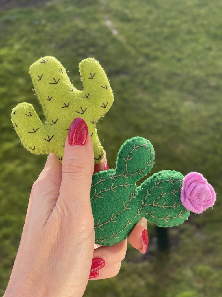 Hand holding felt cactus plushies with embroidered details, showing handmade soft felt toy pieces from cactus pattern project