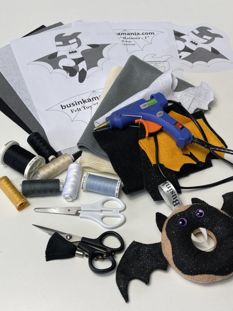 Felt Batman plush sewing materials including soft felt, threads, scissors, and glue gun laid out for craft project preparation
