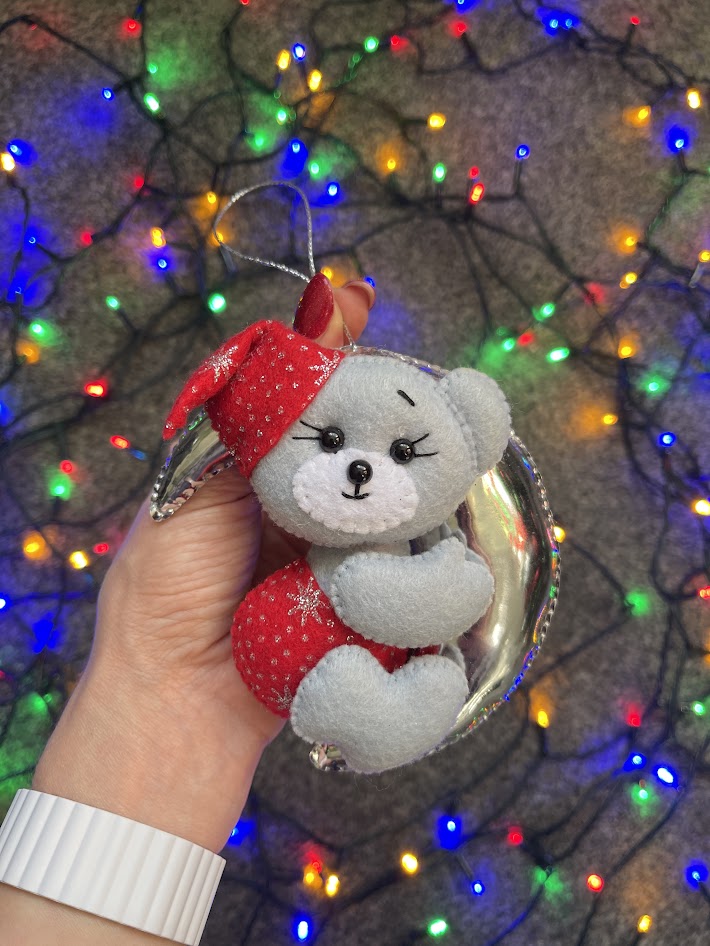 Felt moon bear Christmas ornament with holographic mirrored leather moon and festive fairy lights background