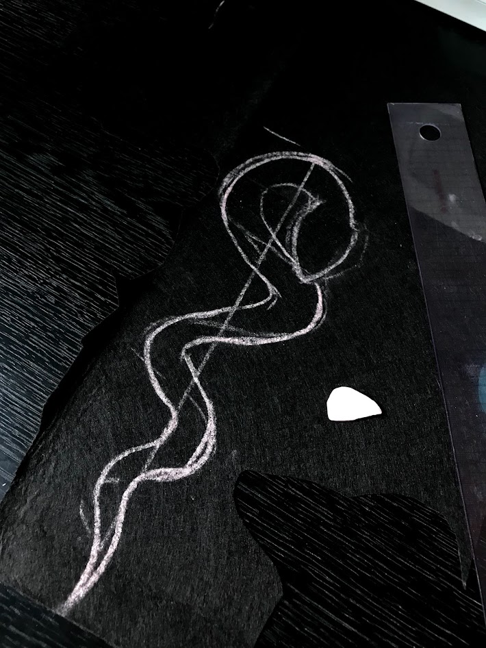 Chalk outline drawn on black felt fabric showing thick uneven pattern lines before cutting plush shapes